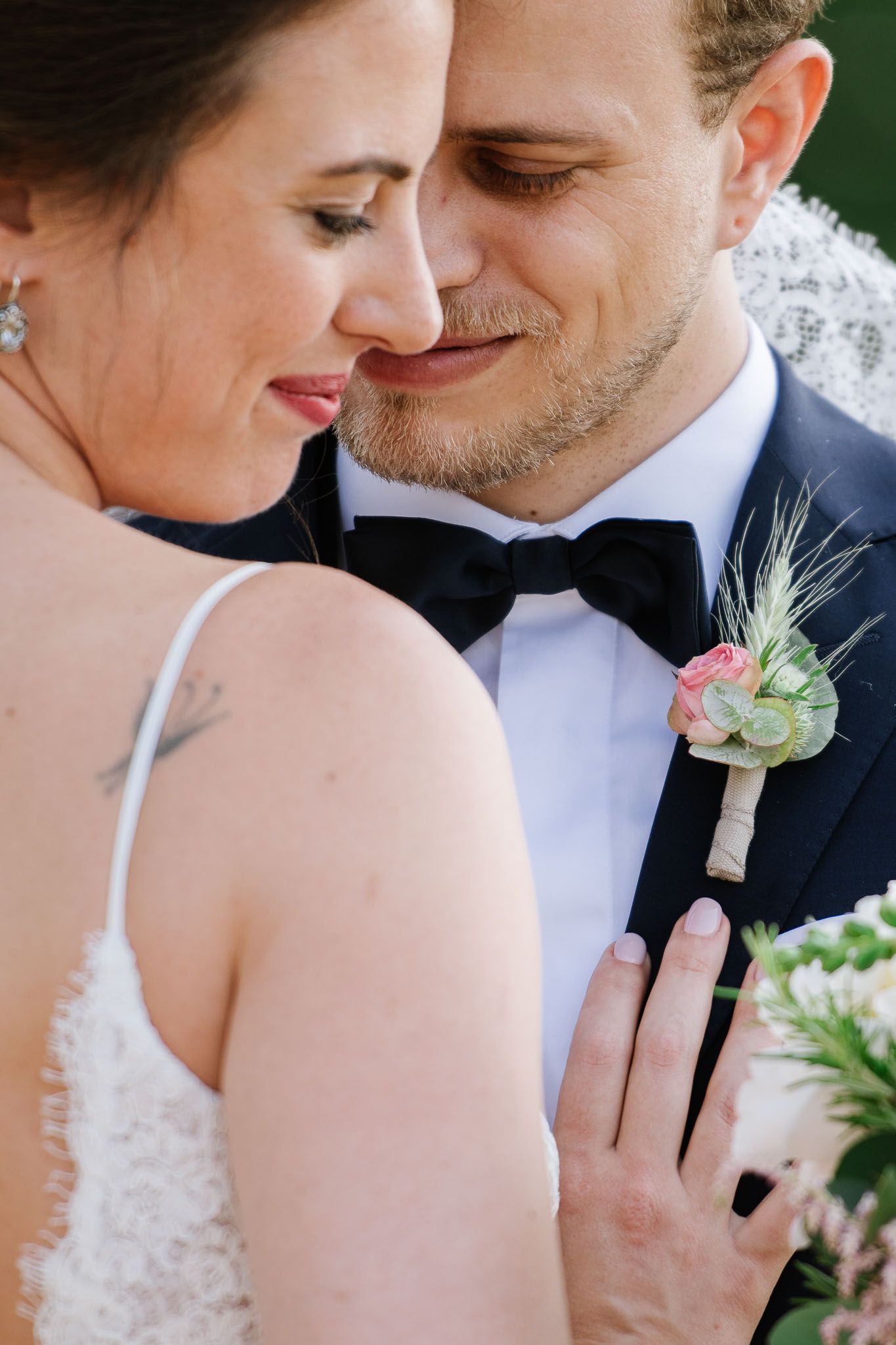 An intimate wedding portrait showing tender moment with elegant attire and boutonniere details.