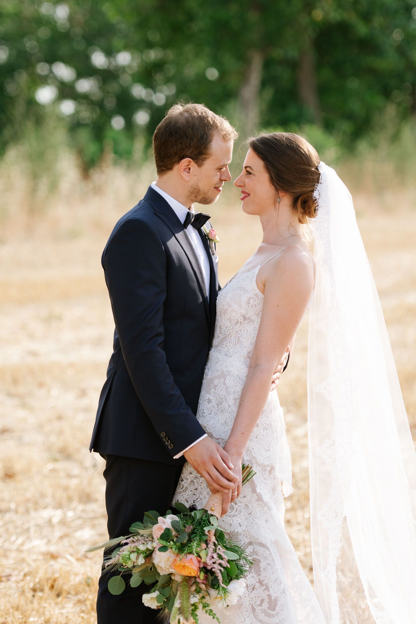 A romantic wedding moment captured in a rustic field with elegant formal attire.