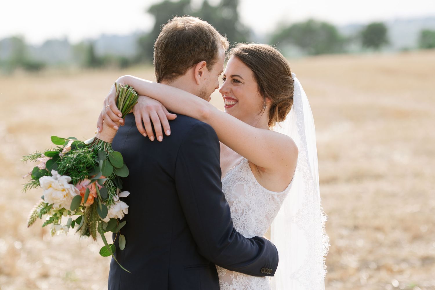 A tender embrace between newlyweds in a golden field with white floral bouquet.