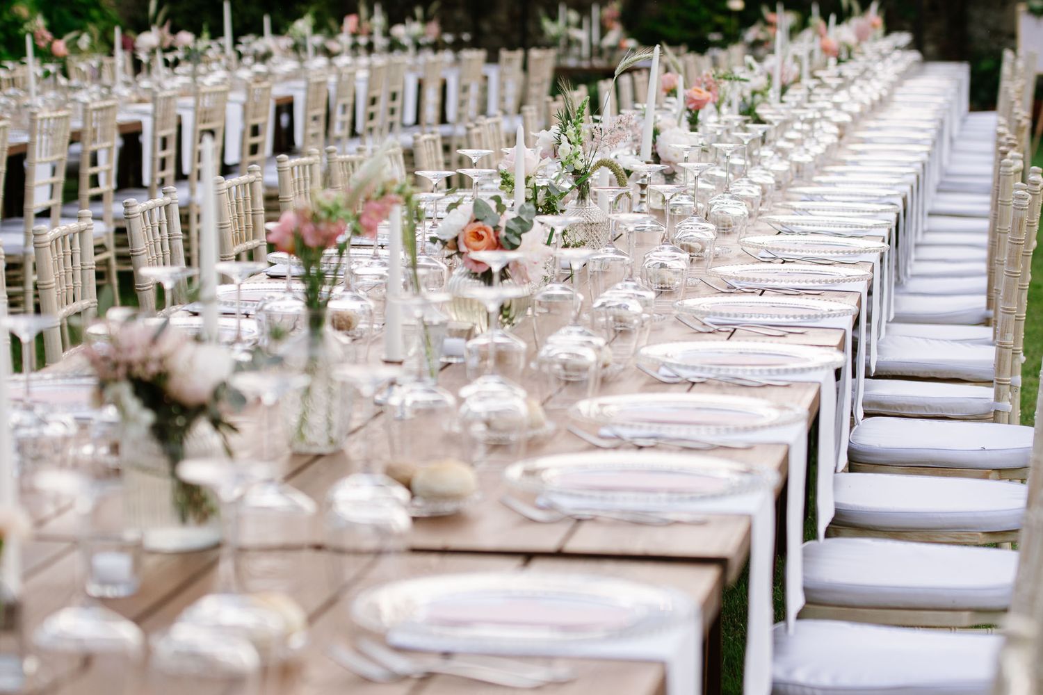 An elegant wedding reception table setting with white chairs and delicate floral centerpieces.
