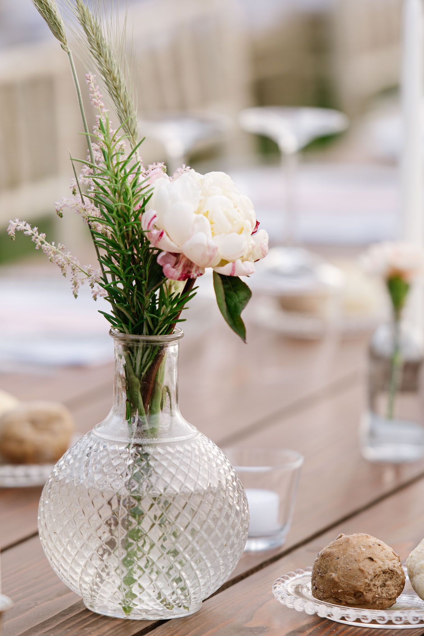 A delicate peony flower arrangement in a cut glass vase with greenery on a wooden table.