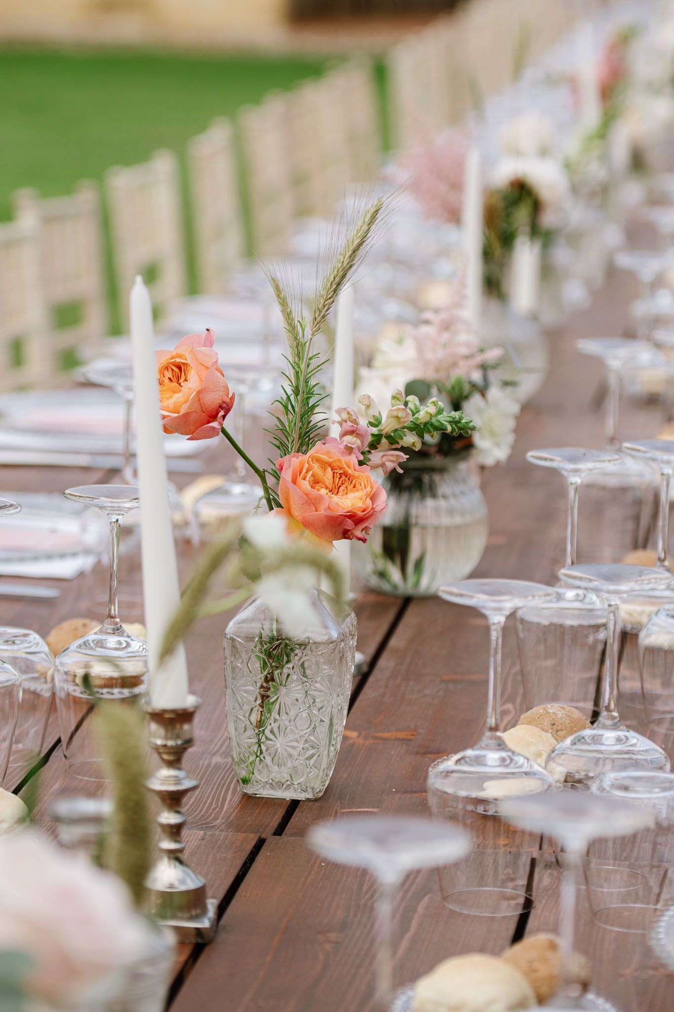 Wedding table decorations featuring peach roses and glass vases on rustic wooden tables.