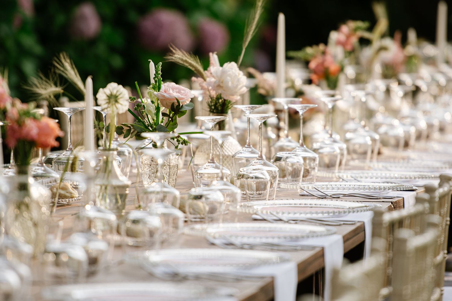 Elegant table setting with delicate floral arrangements and candles for an outdoor wedding reception.