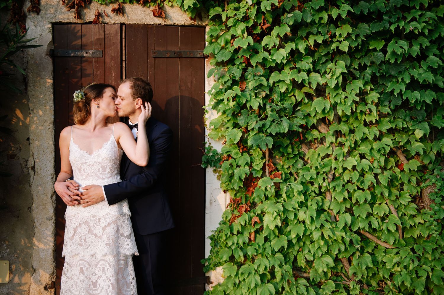 Bride and groom share romantic moment against rustic door with ivy covered walls.