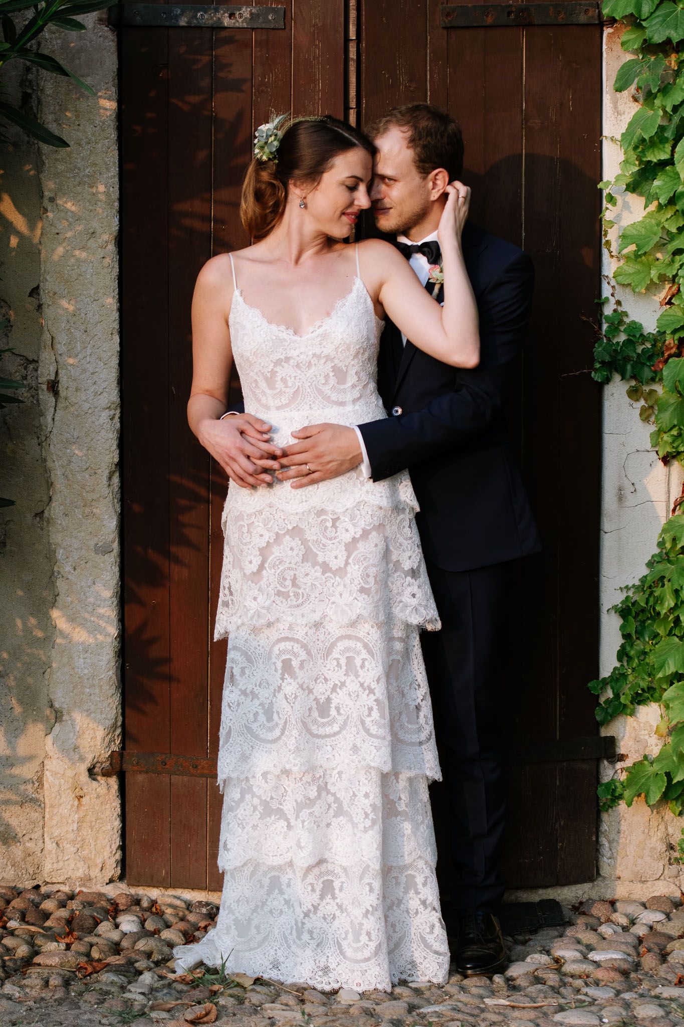 Couple in wedding attire embracing by vintage wooden door with climbing vines.
