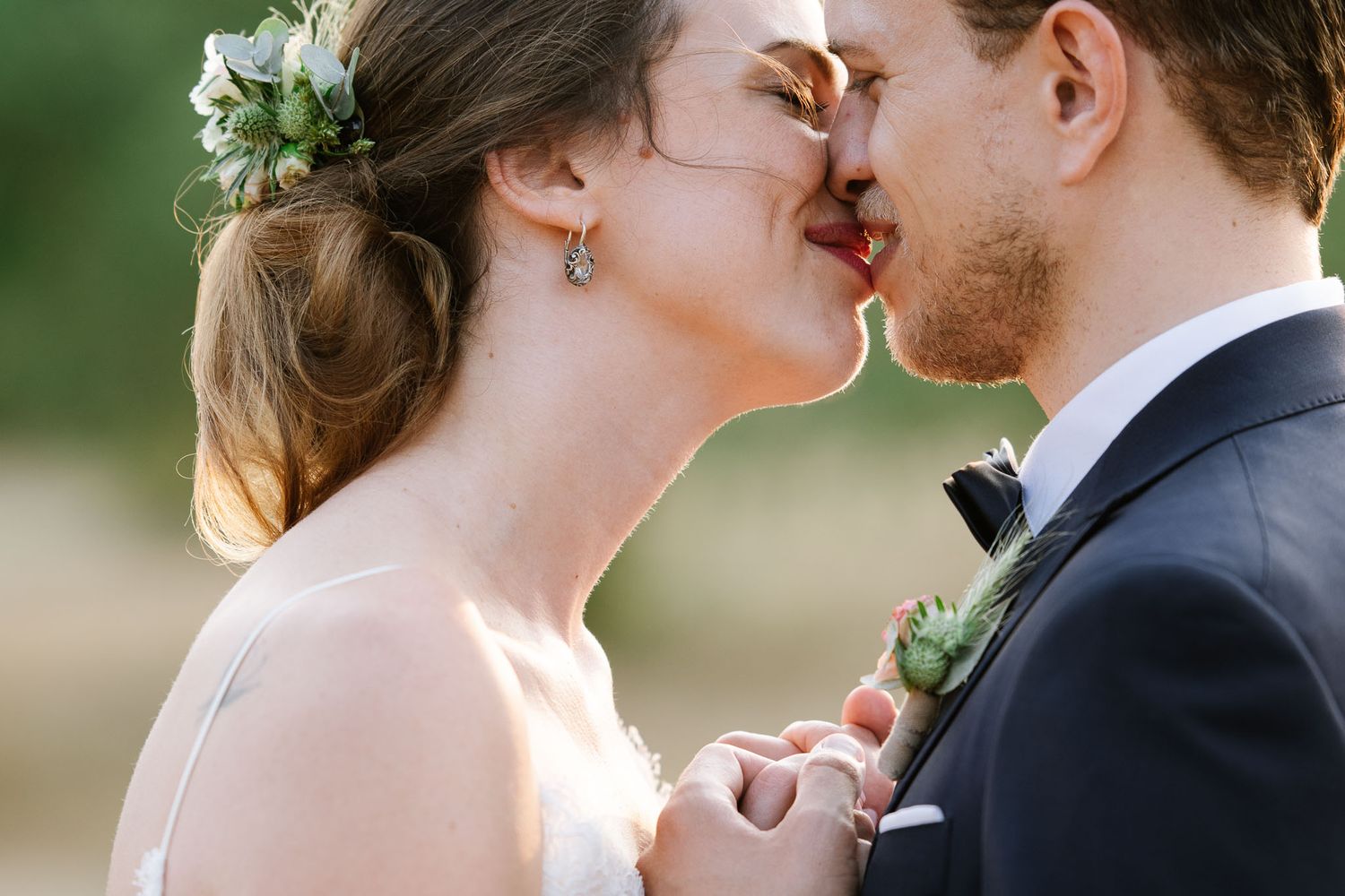 Intimate moment between newlyweds with floral hair accessories in natural setting.