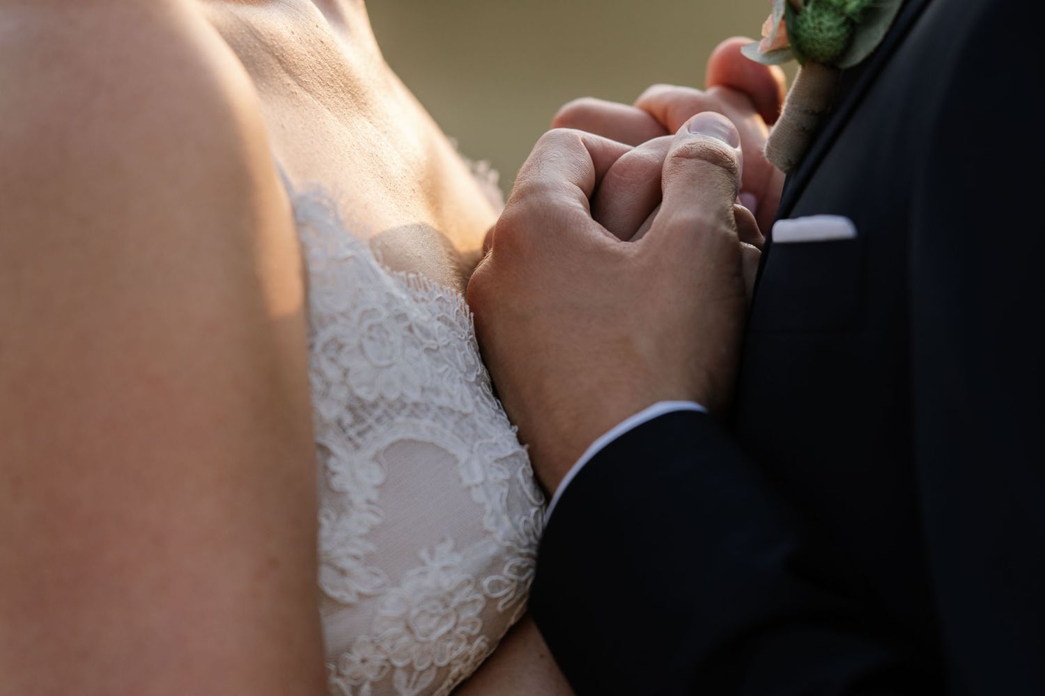 Close-up of couple holding hands showing wedding rings and lace dress details.