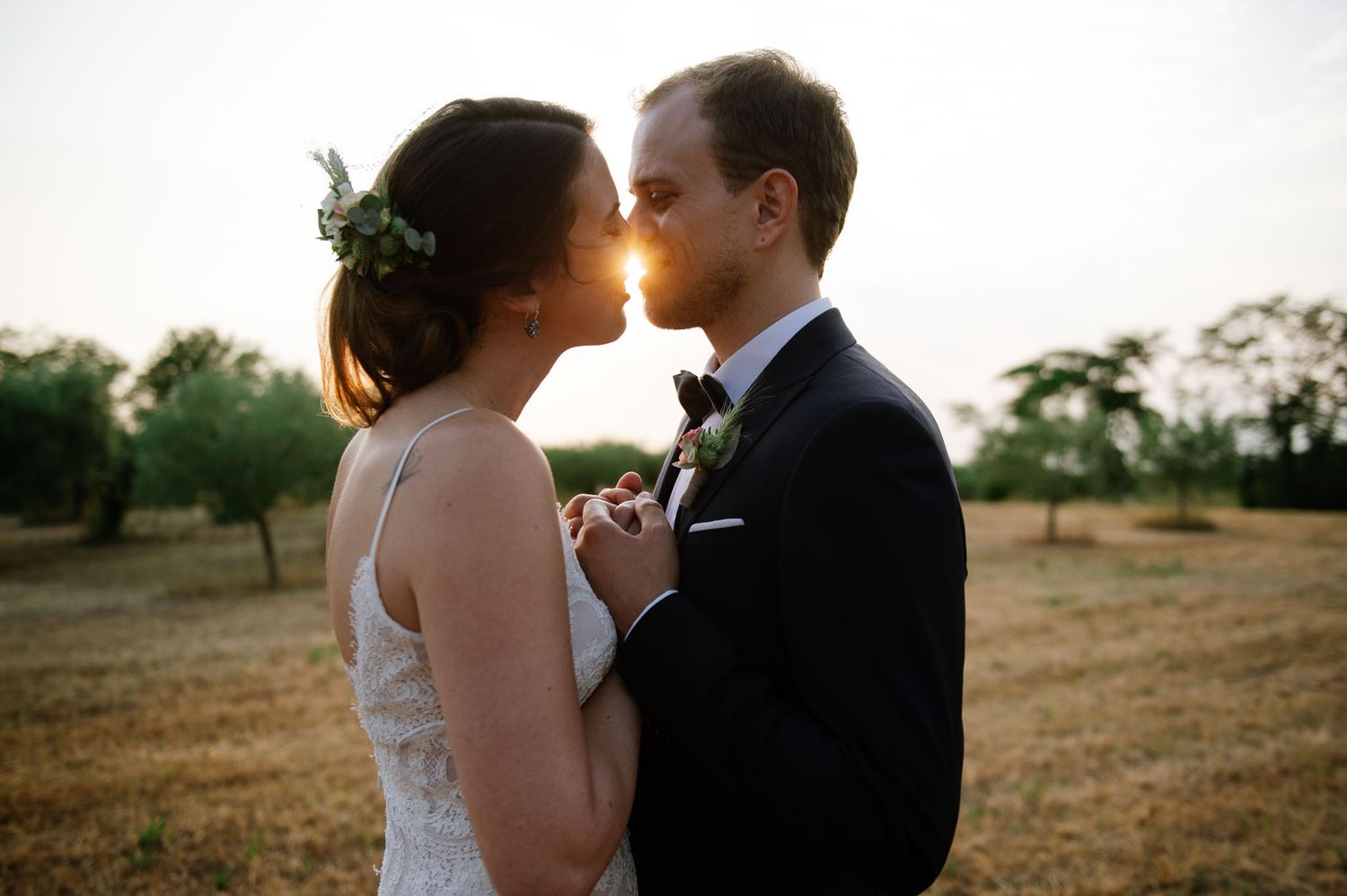 Romantic sunset portrait of couple in wedding attire in rustic field setting.