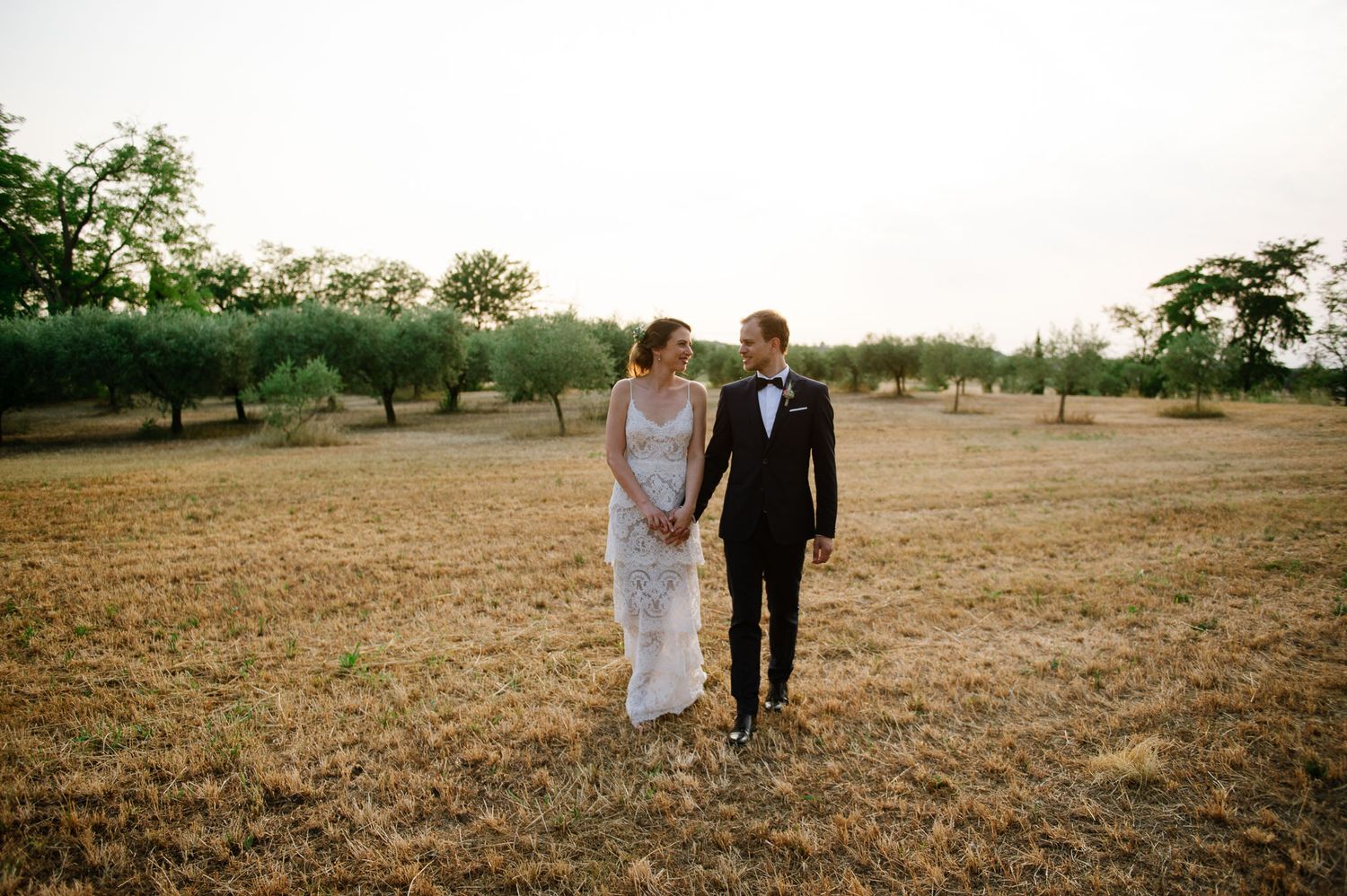 A couple strolls through a sunlit field during golden hour at their wedding.