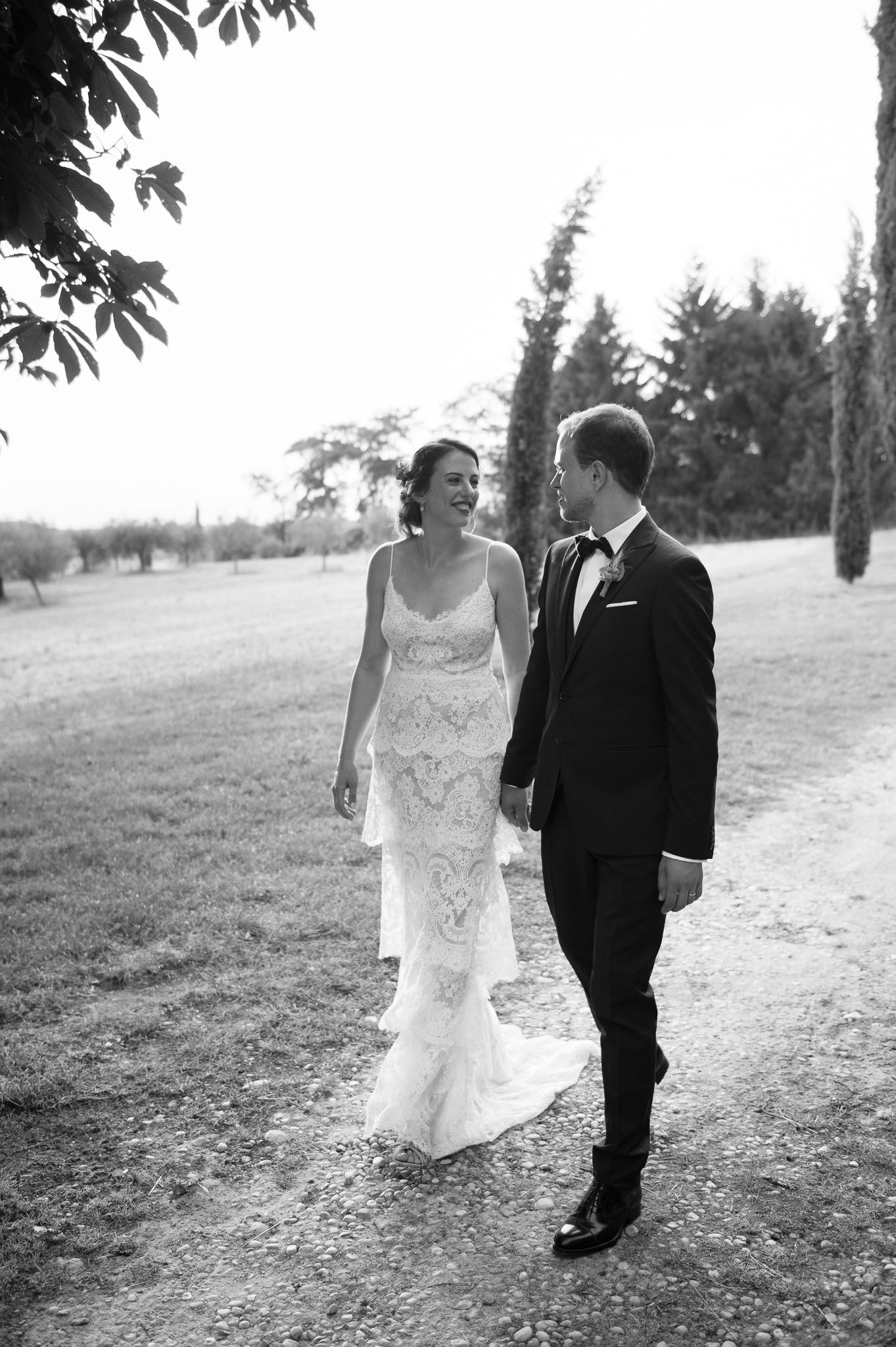 Black and white portrait of newlyweds walking along a cypress-lined path.
