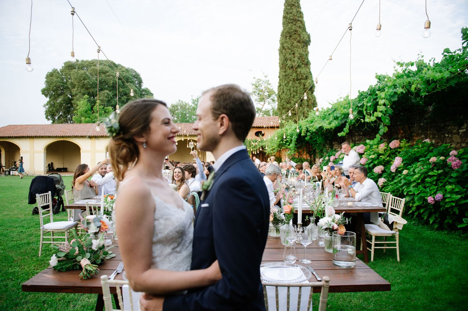 Wedding reception scene with string lights and guests seated in an elegant garden setting.
