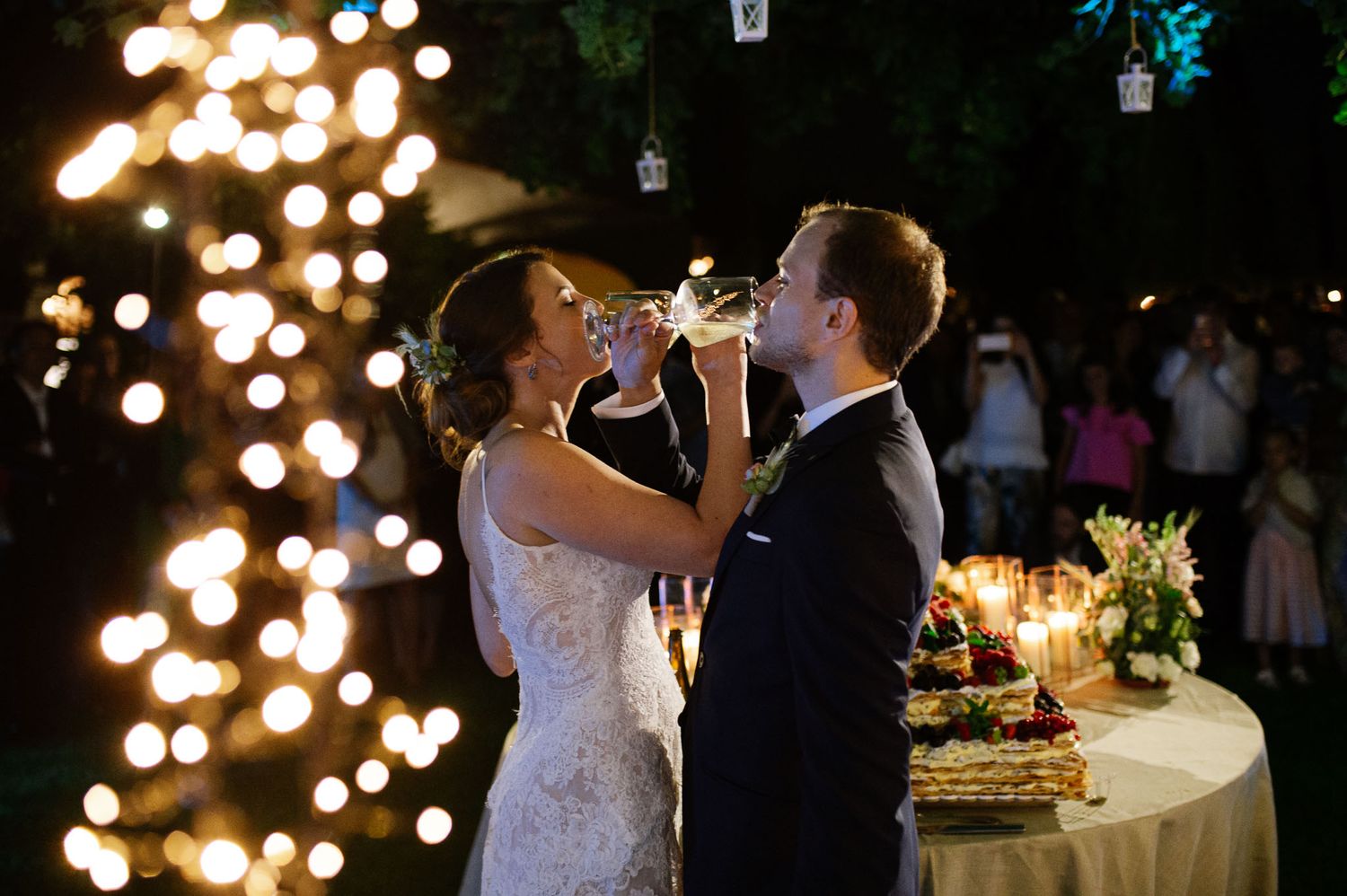 A romantic moment shared during a wedding reception with string lights and bokeh effects in the background.