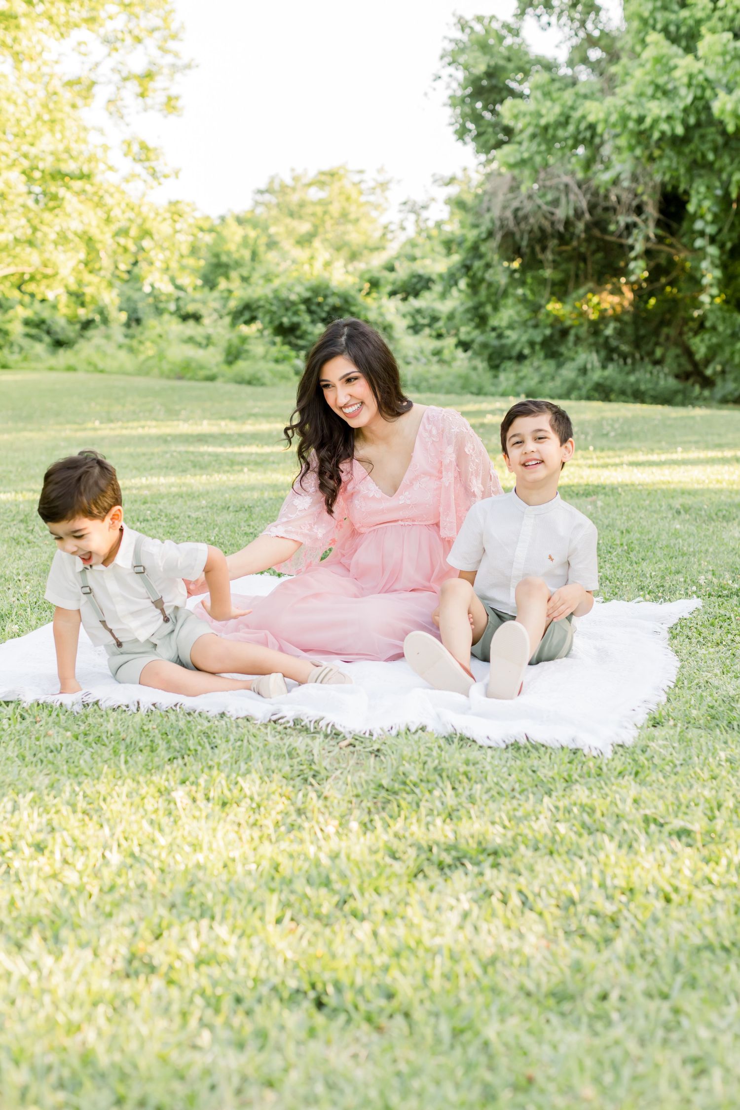 A candid family photo shows three people sitting together on a white blanket in a park.
