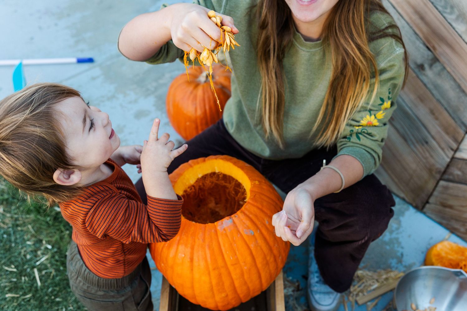 People removing seeds and pulp from a large orange pumpkin outdoors.
