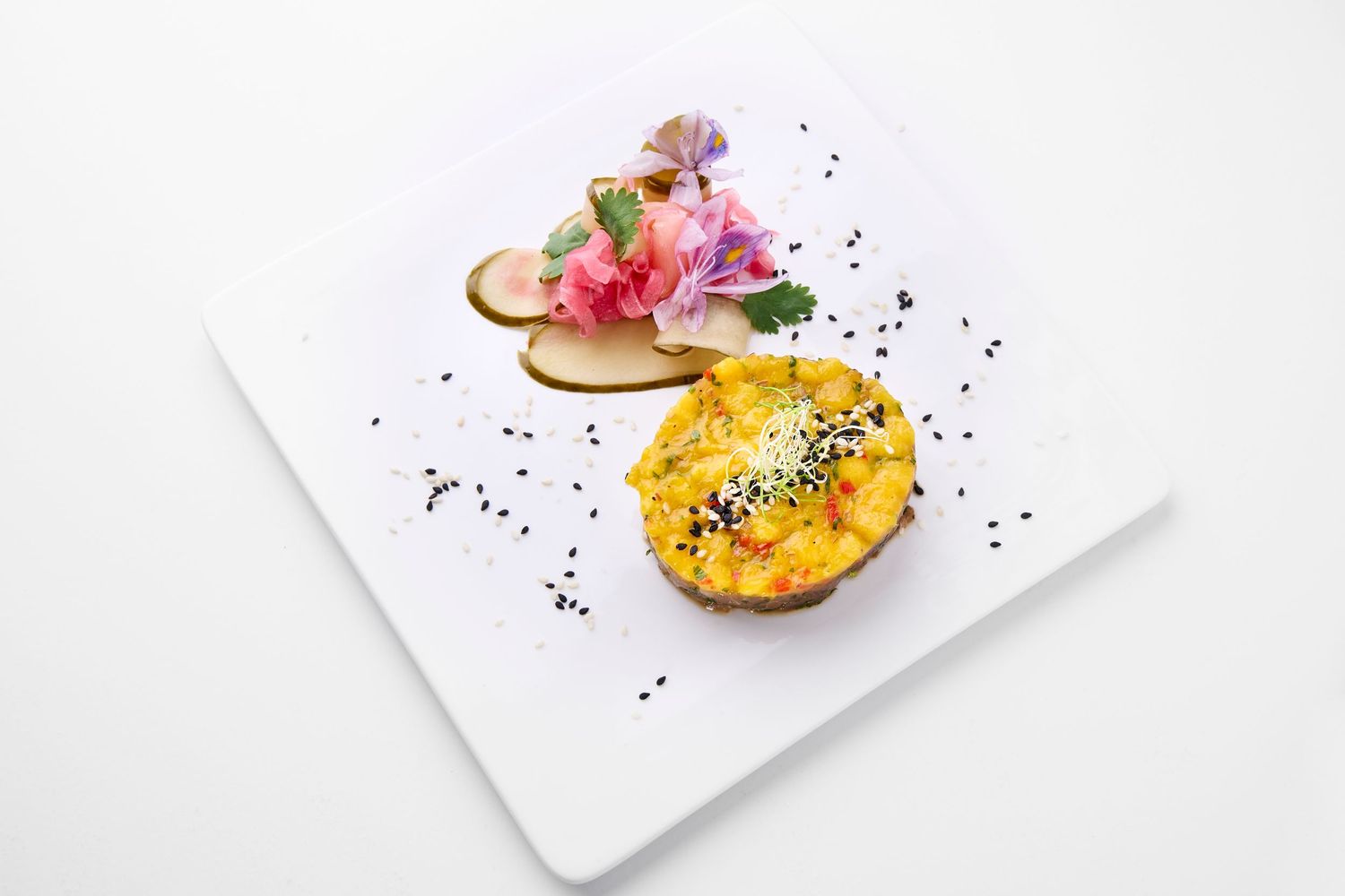 Minimalist plated dessert with yellow and pink garnishes on white dish.