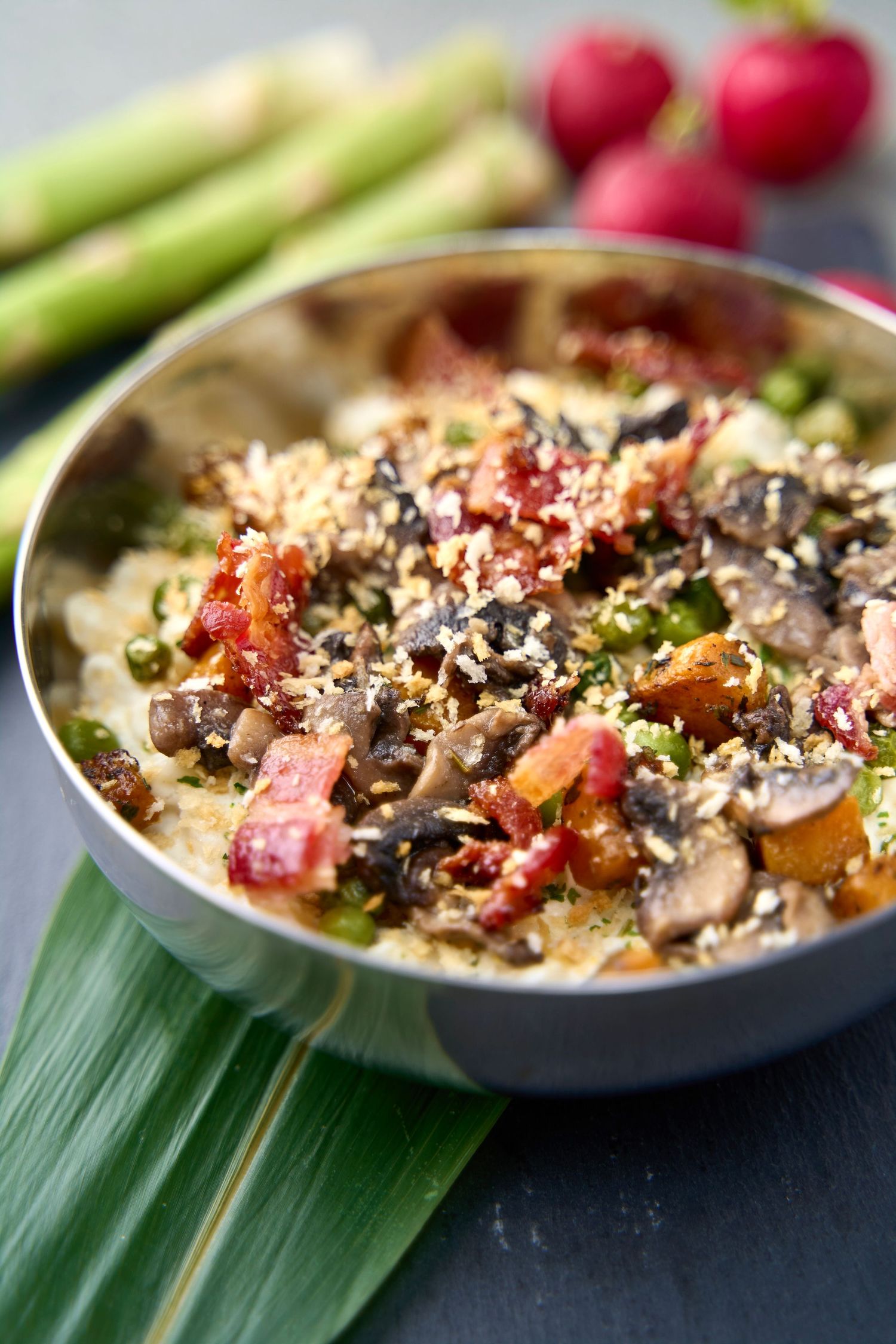 Hot appetizer with mushrooms, bacon and sesame seeds served on a green banana leaf.