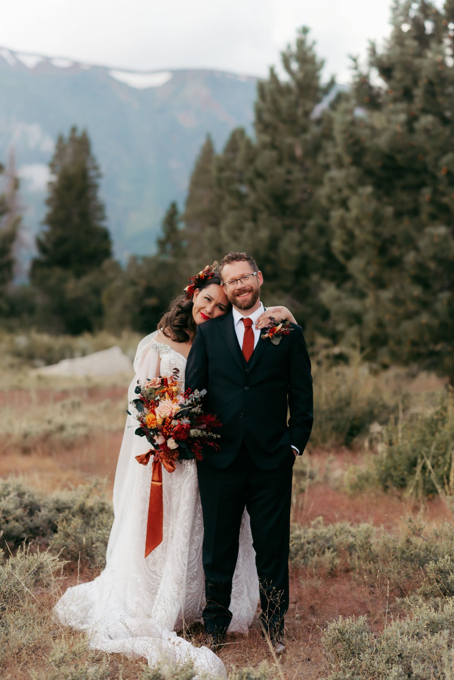 A scenic mountain wedding portrait with a colorful autumn bouquet against snow-capped peaks.