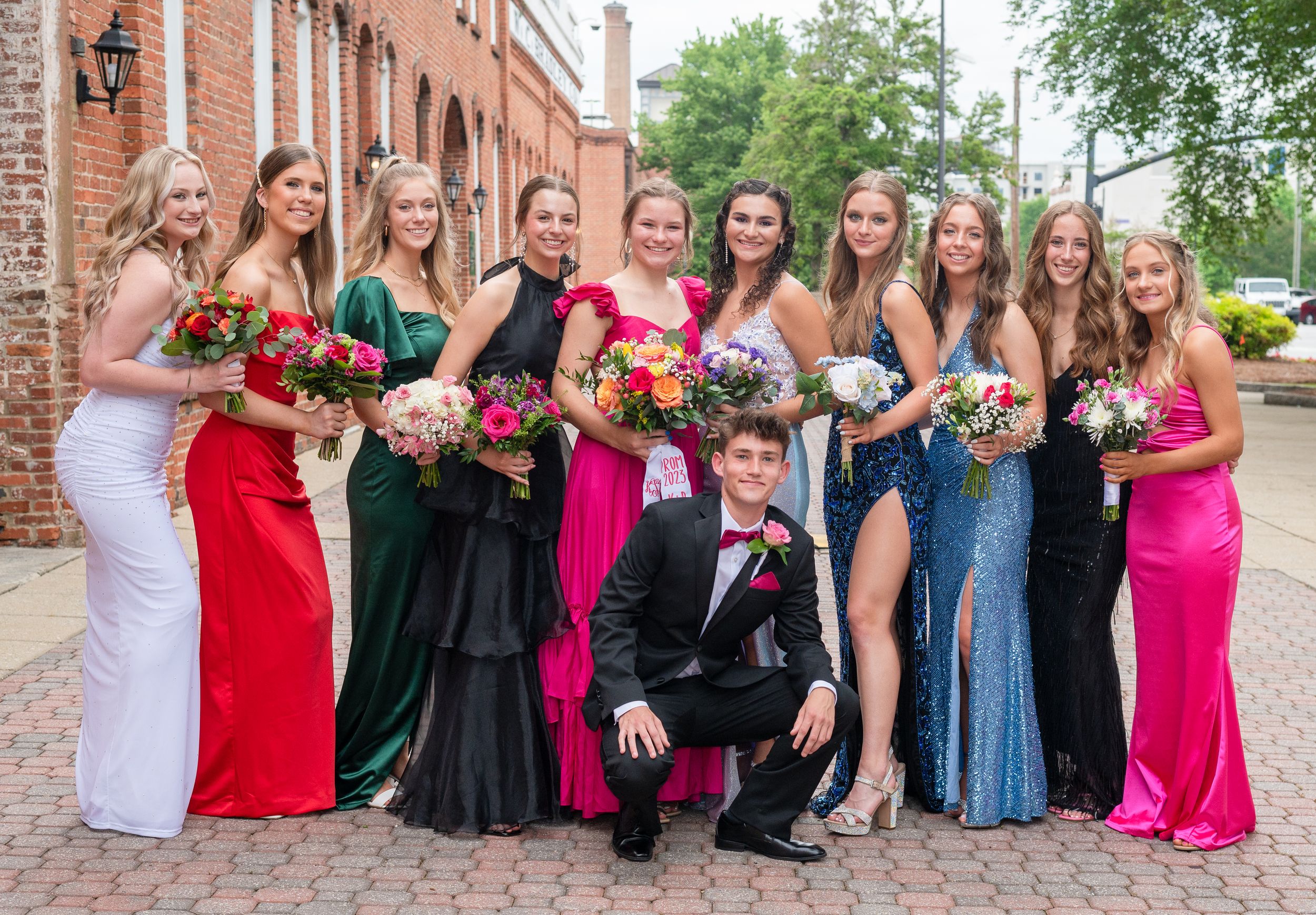 Formal group photo of prom or homecoming attendees in colorful gowns.
