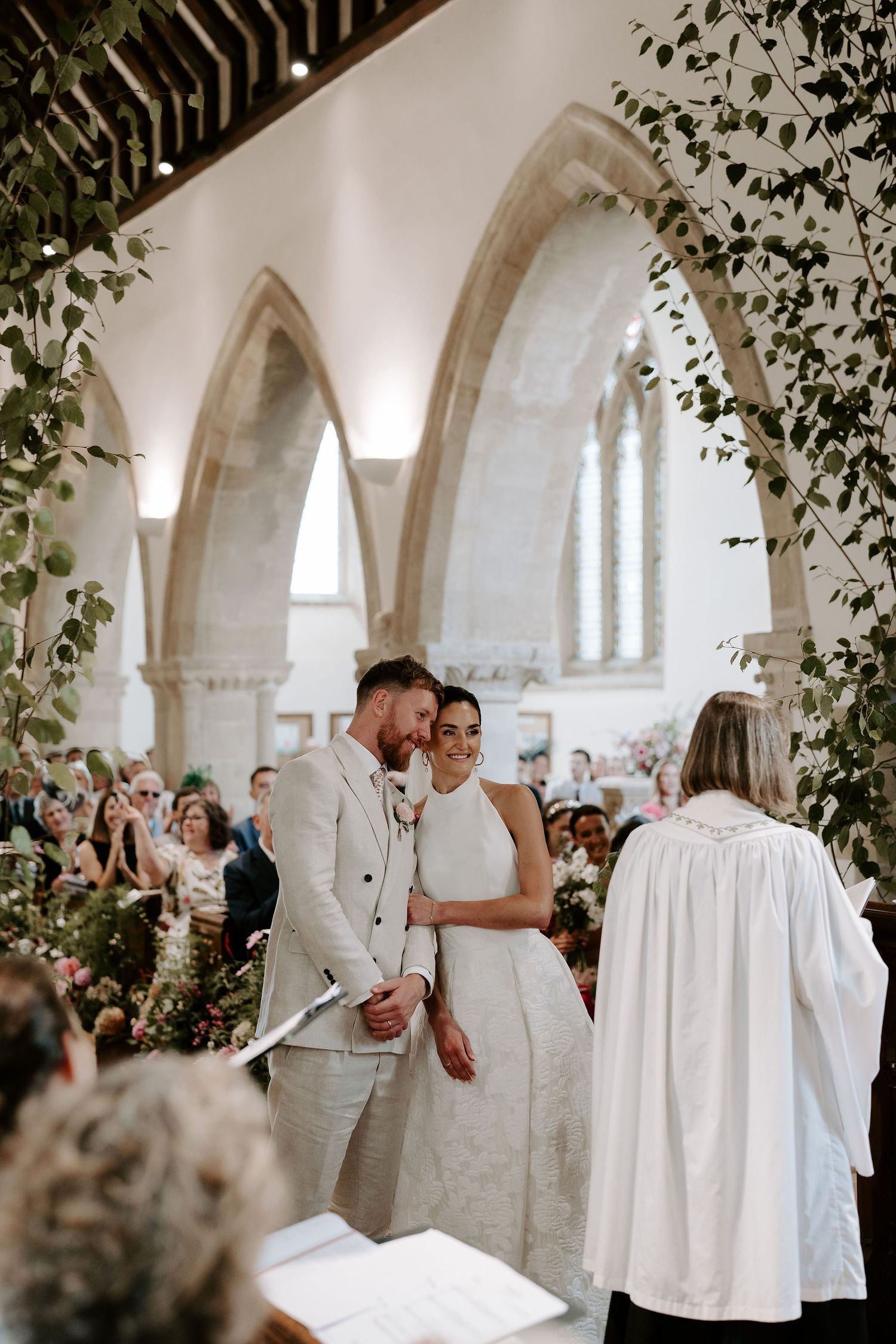 bride leaning into the groom smiling as she holds his arm during the ceremony at st Nicholas church in Oxfordshire