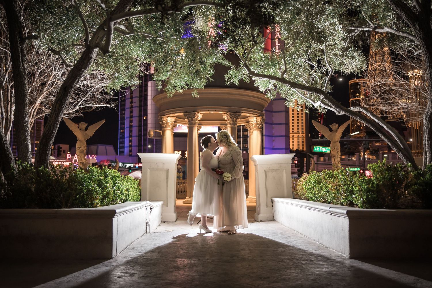 Romantic wedding portrait at night under decorated archway with ambient lighting.