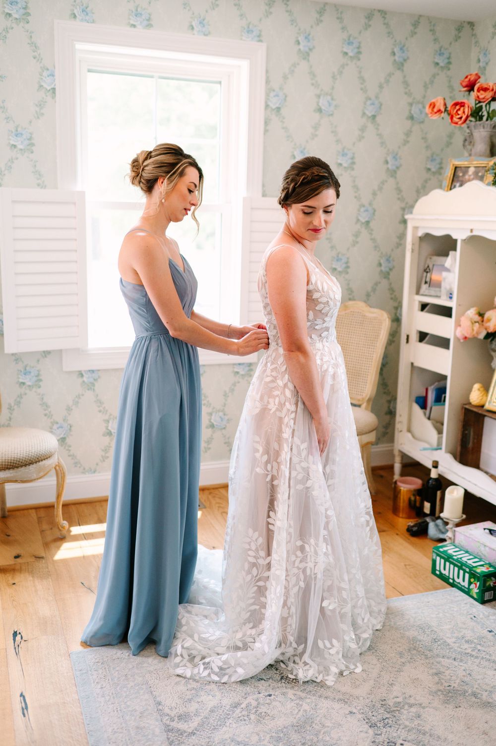 Wedding preparation scene in a room with blue floral wallpaper and white furniture.