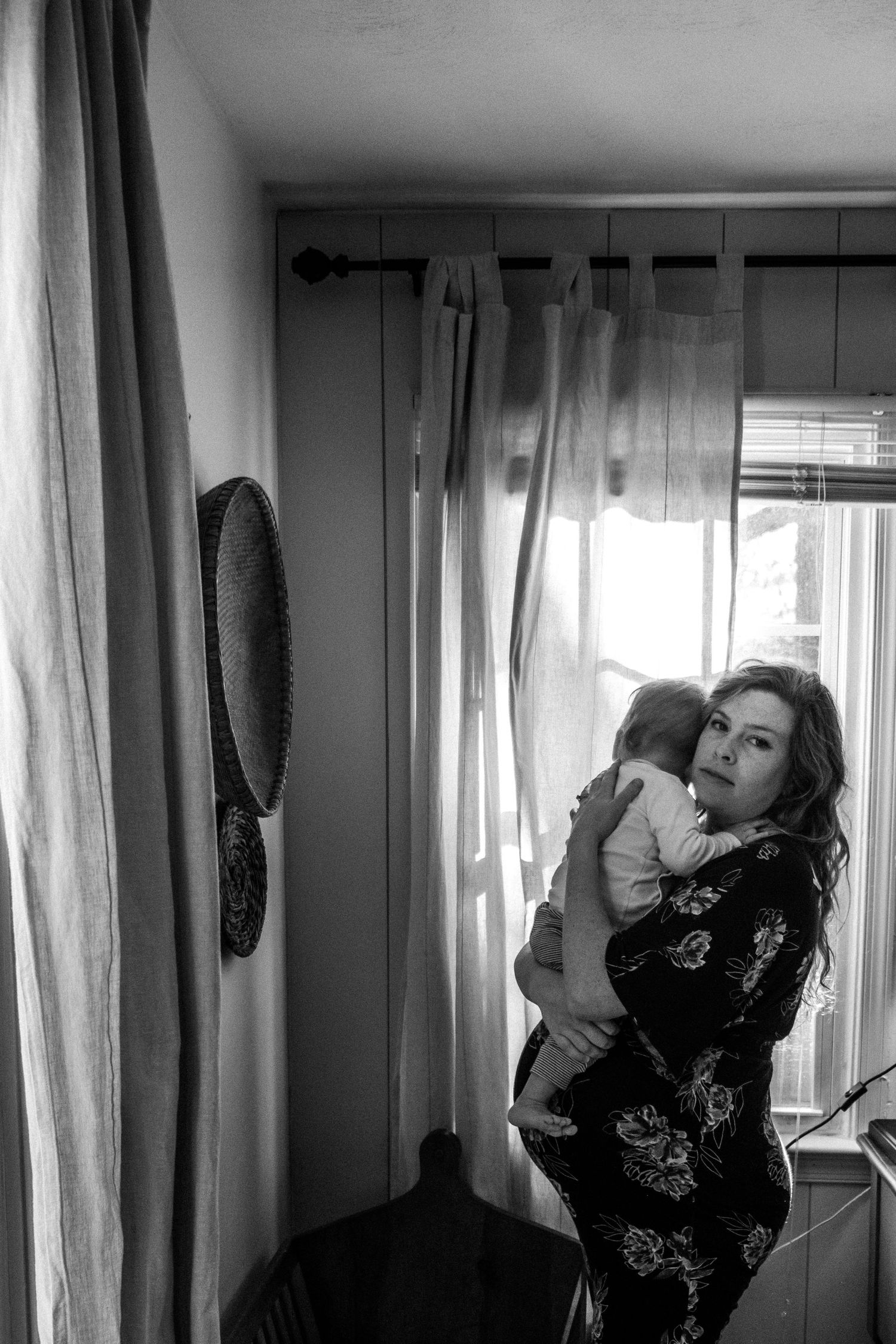 pregnant mother holding baby and making direct eye contact with the camera in her home