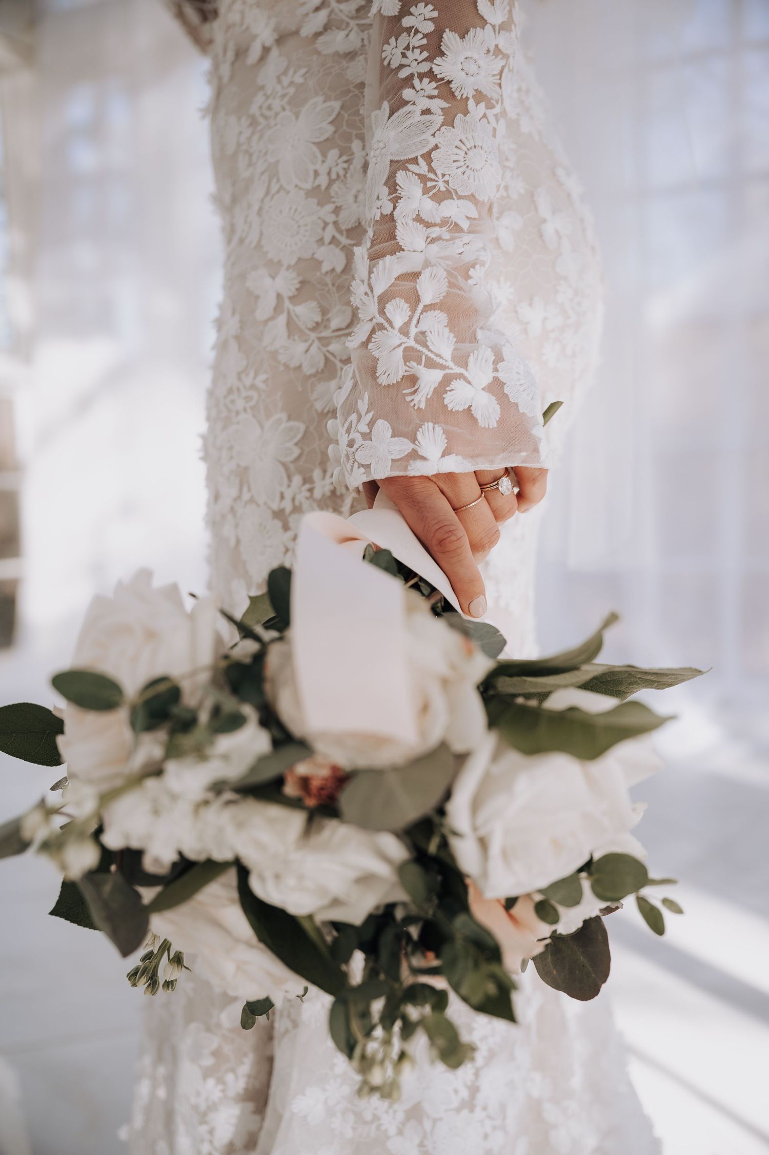 Close-up of white bridal bouquet with roses against lace wedding dress detail.