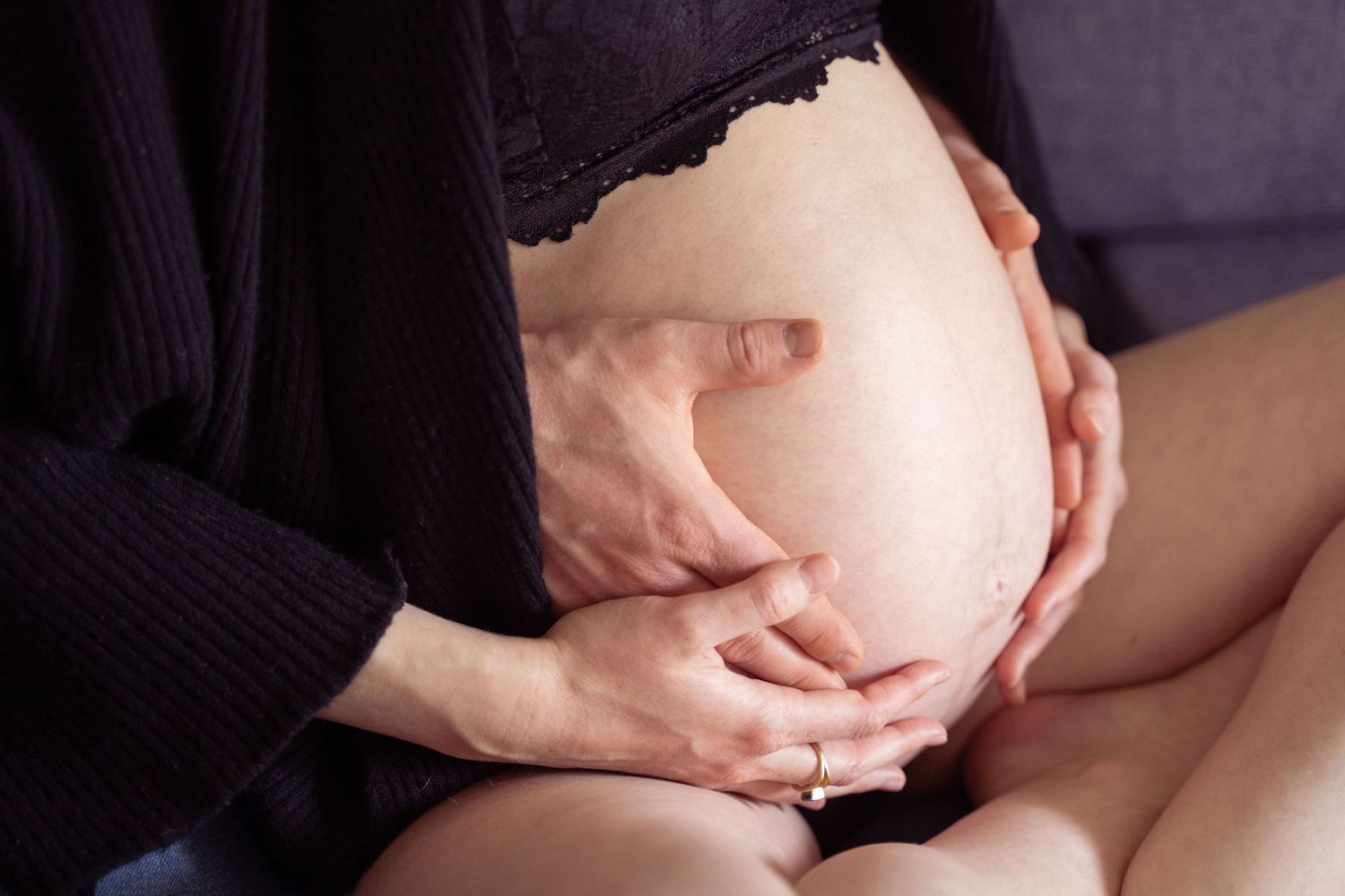 Close-up of pregnant belly being gently cradled by two pairs of hands during maternity photoshoot.