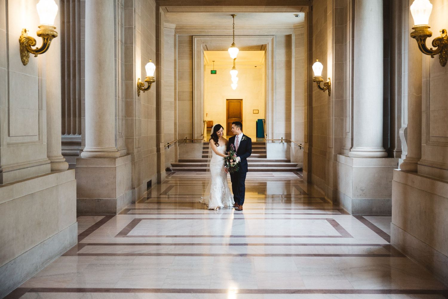 A elegant wedding portrait in a bright marble hallway with classical architecture.