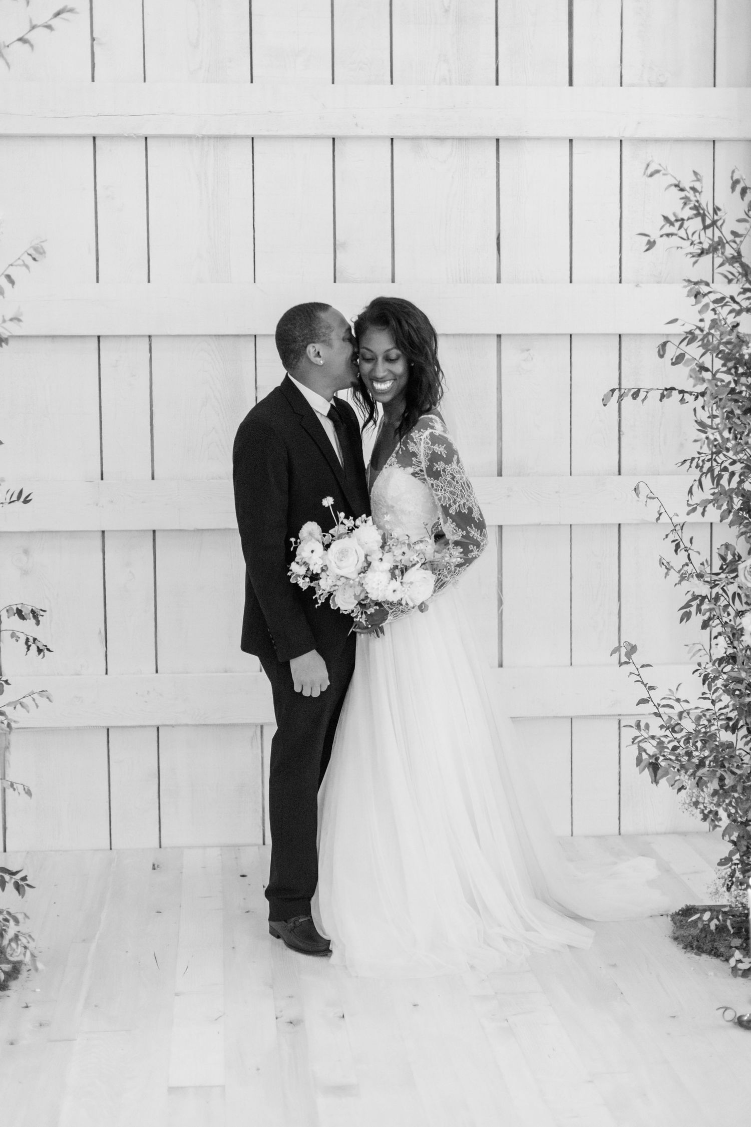 Wedding couple photographed in elegant poses against white wooden wall background.
