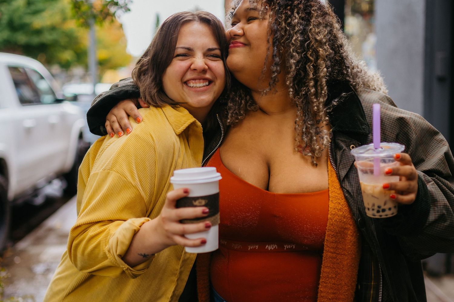 Two friends sharing drinks and laughter together in casual attire on a sunny day.