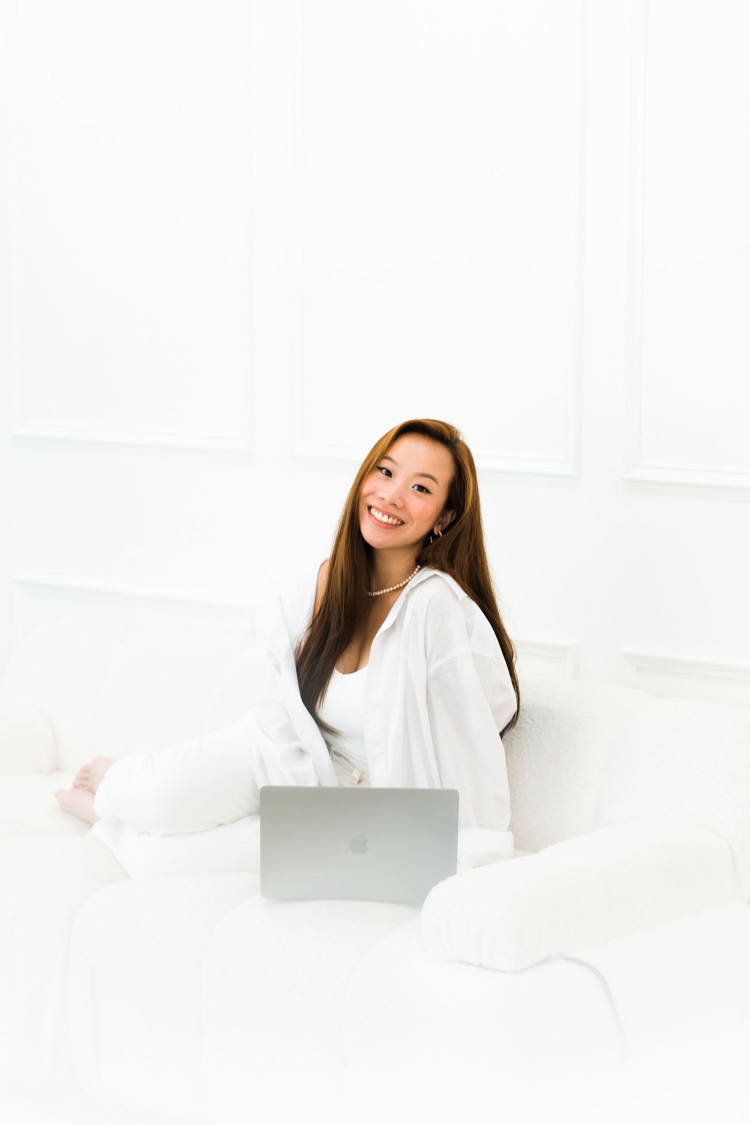 Woman in white loungewear relaxing with laptop on cozy bed.