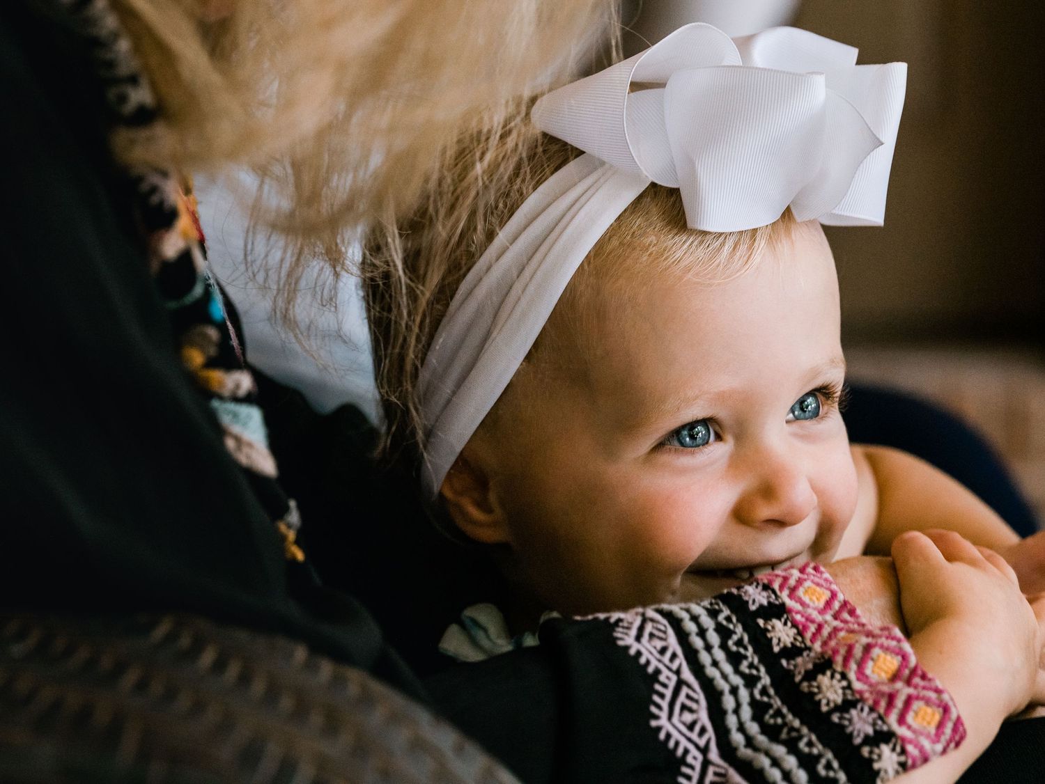 toddler girl in large white bow holding on to parents arm