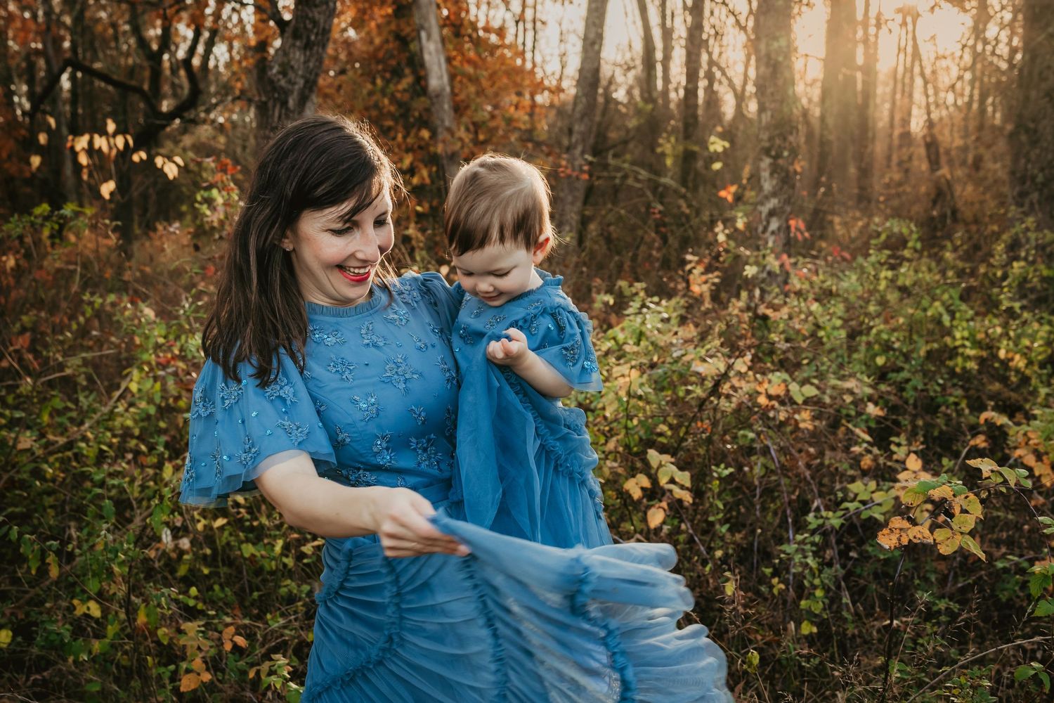 A joyful moment shared in matching blue outfits against an autumn forest backdrop.