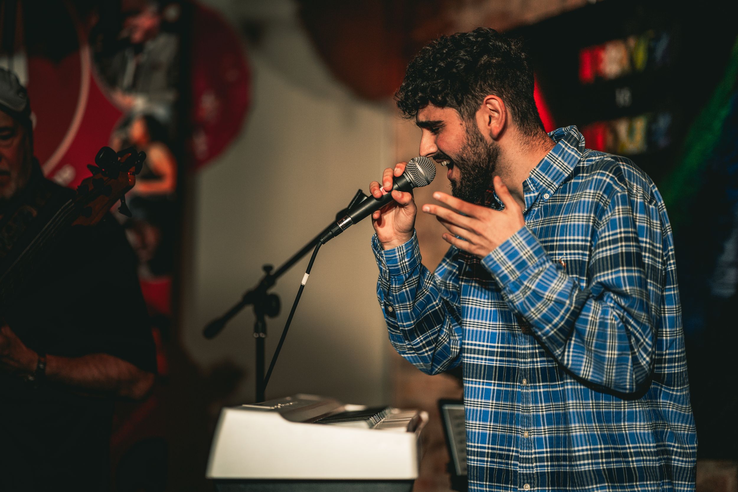 Performer in a plaid shirt singing into a microphone during a live show.