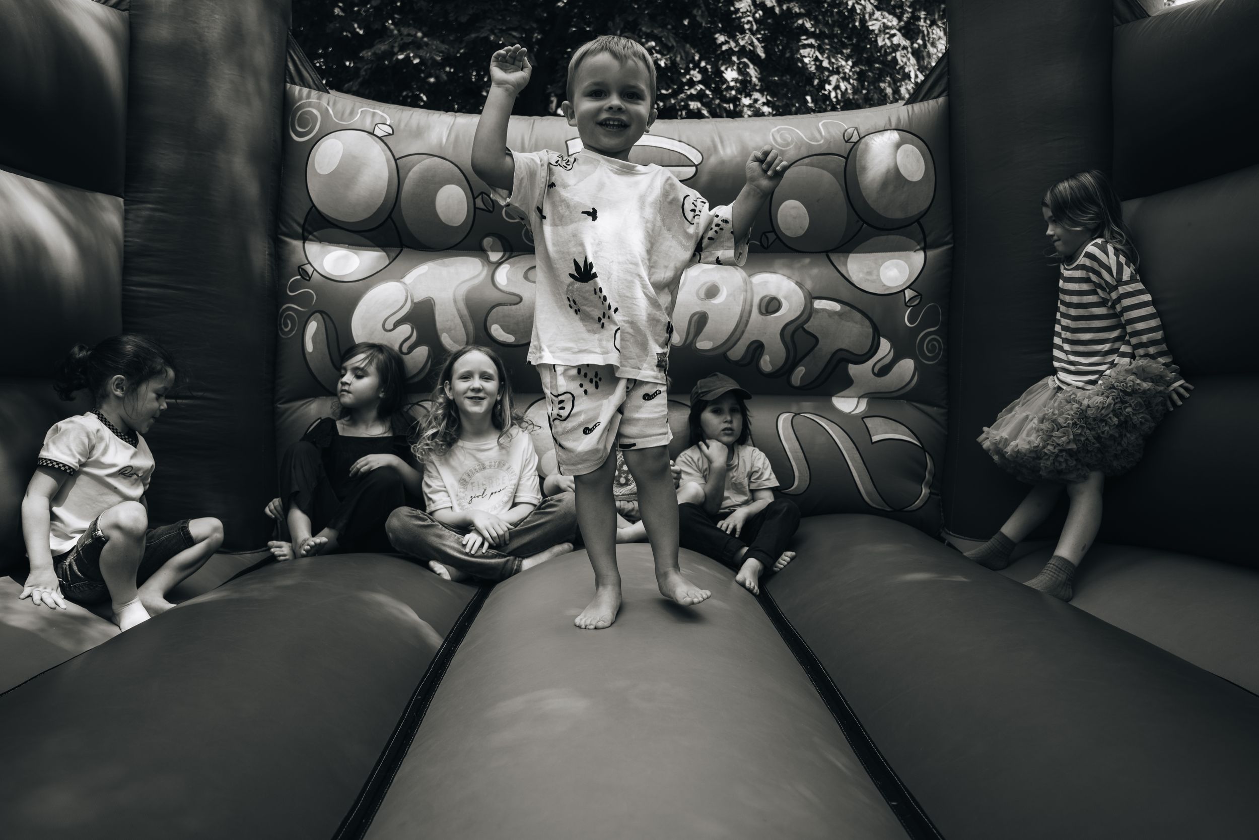 Black and white photo of children sitting in a bounce house at a party.