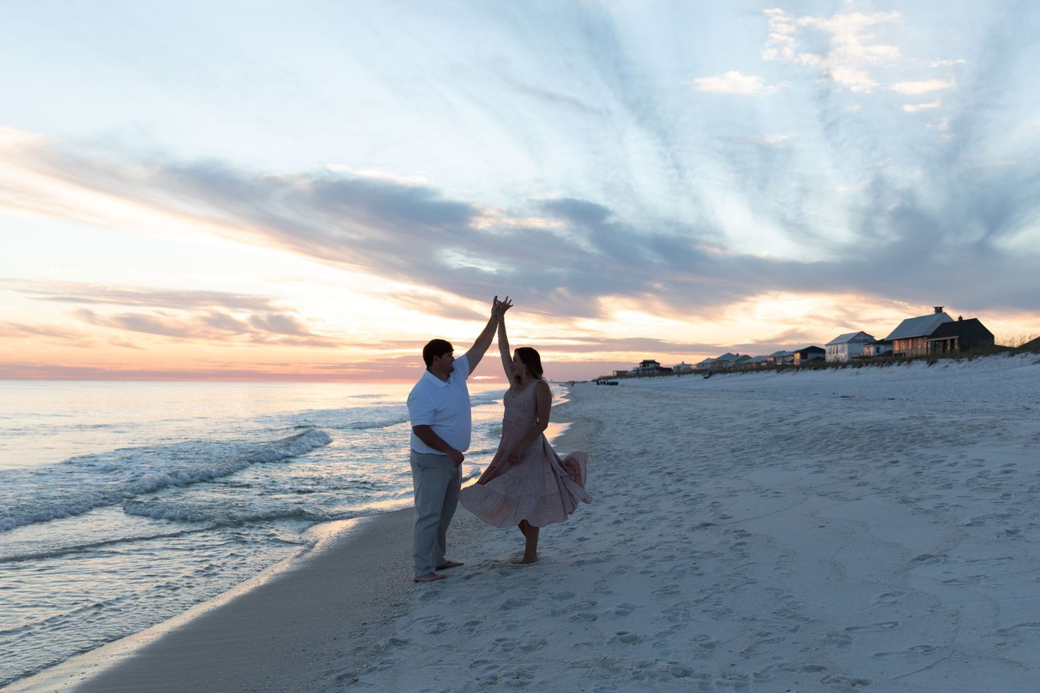 Silhouetted couple dancing on beach during golden sunset with ocean waves rolling in.