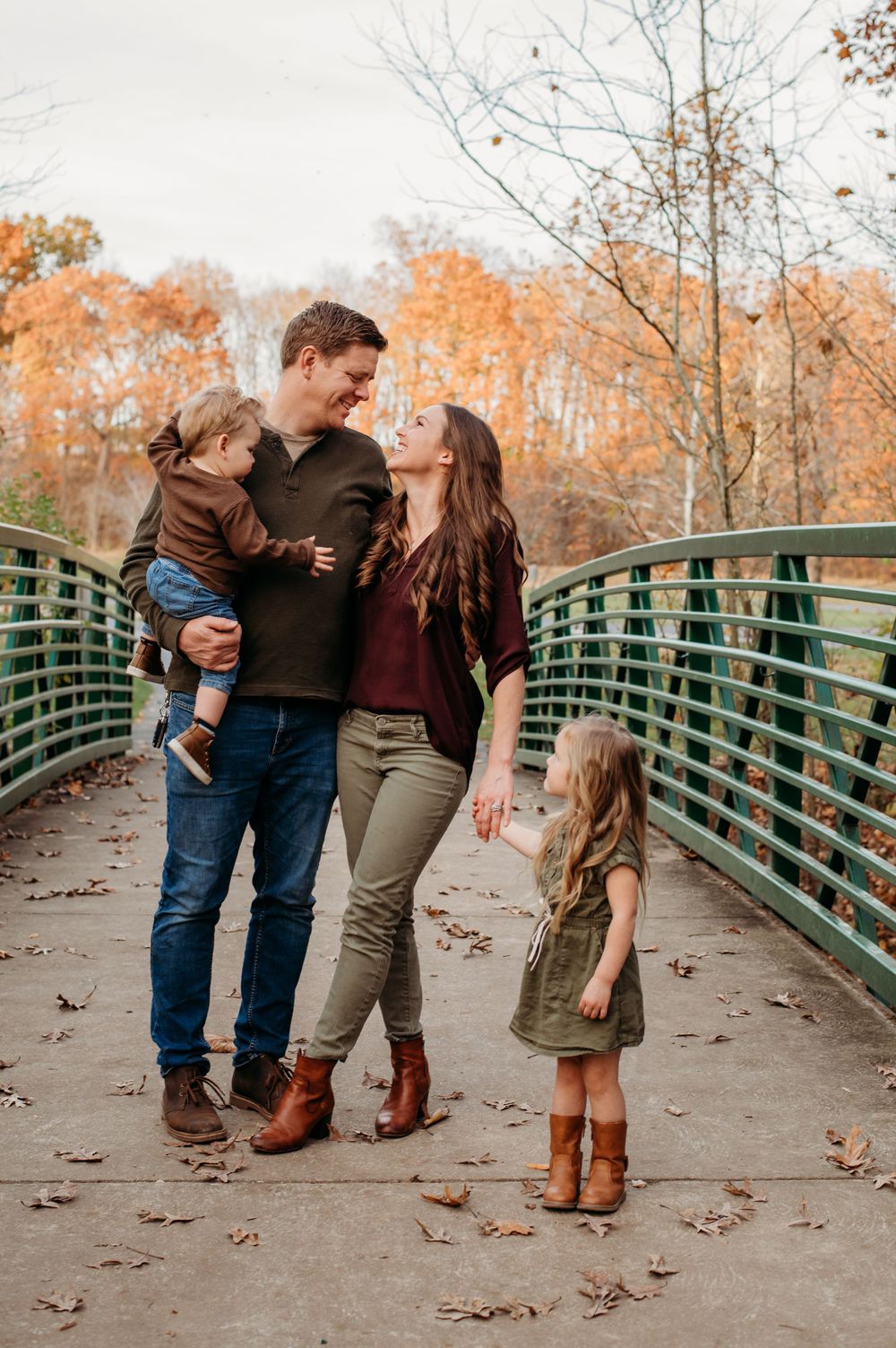A family is standing on a bridge in St. Charles county holding hands and smiling at each other while having their family photo taken.