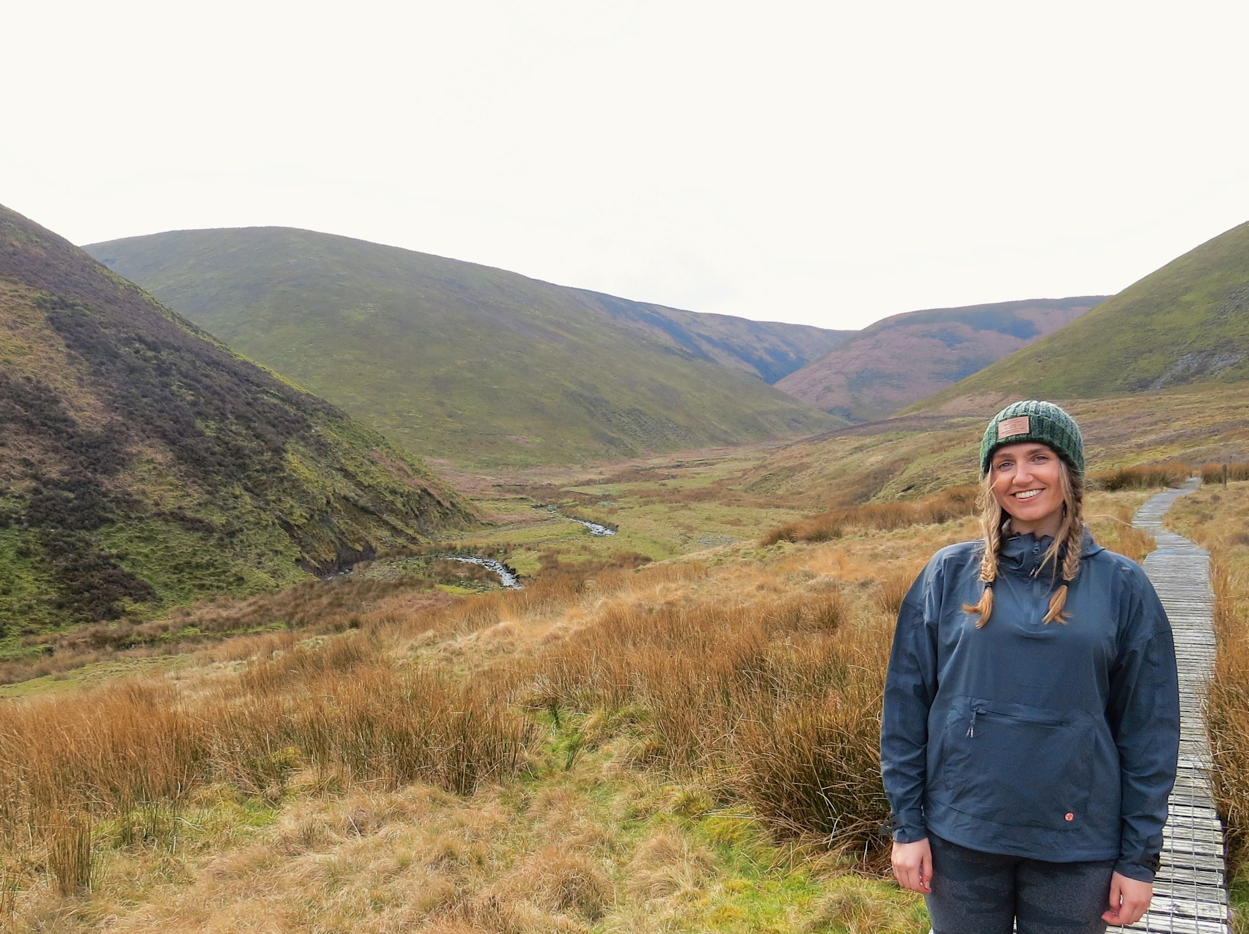 Hiker on trail overlooking dramatic valley in misty mountain landscape.