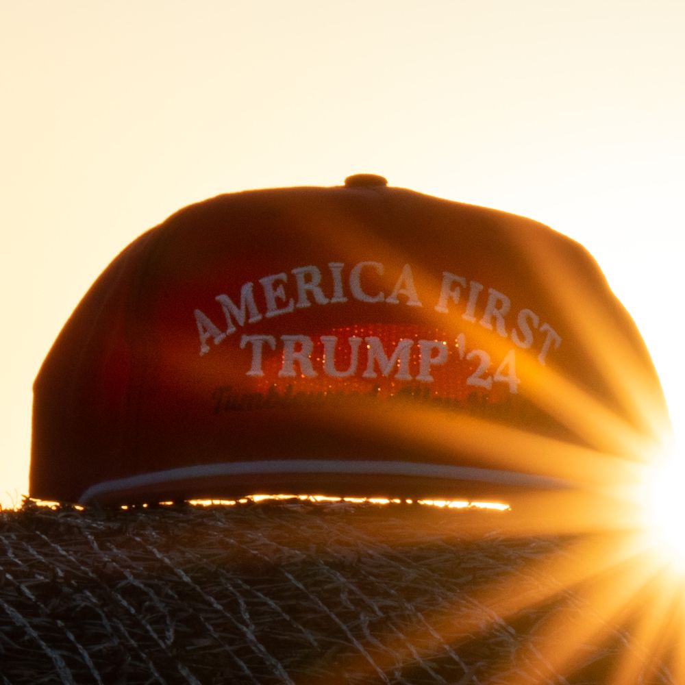 Orange America First Trump hat silhouetted against bright sunlight.