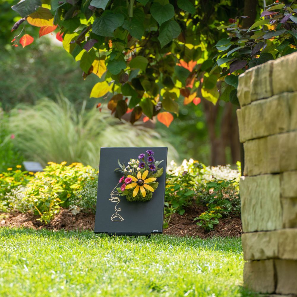 Outdoor garden display of black canvas art featuring fresh flowers and delicate line drawings.