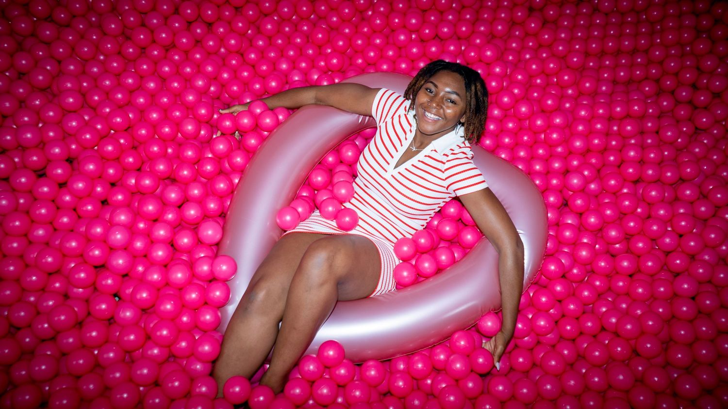 Person lounging on pink inflatable ring against bright patterned background.