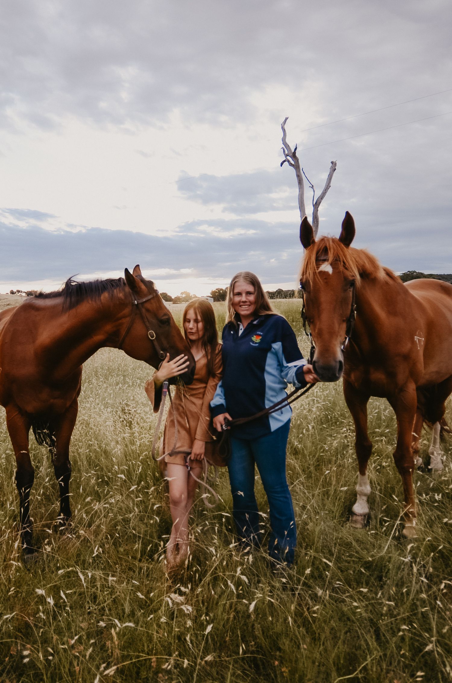 two girls in a rural landscape with horses, and long grass.