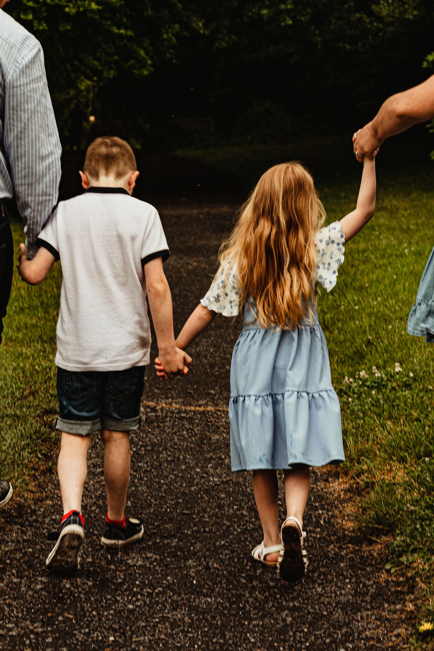 Brother and sister holding hands with parents on walk in woods