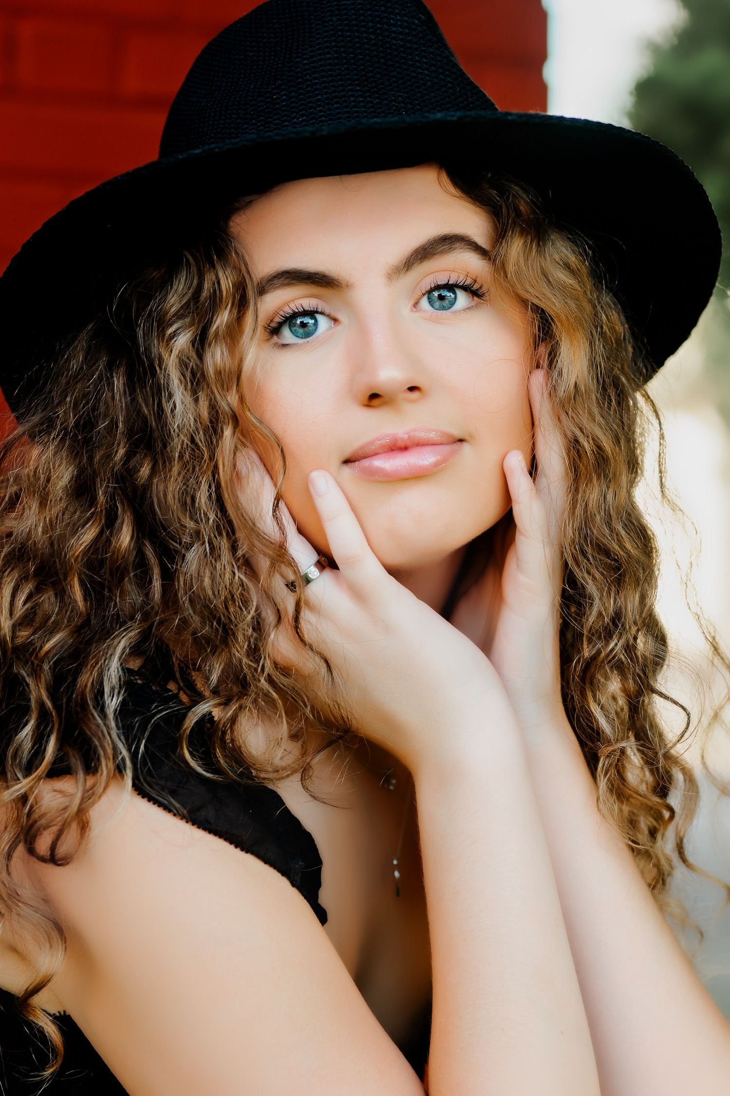 A close-up portrait featuring curly hair and a black hat against a neutral background.