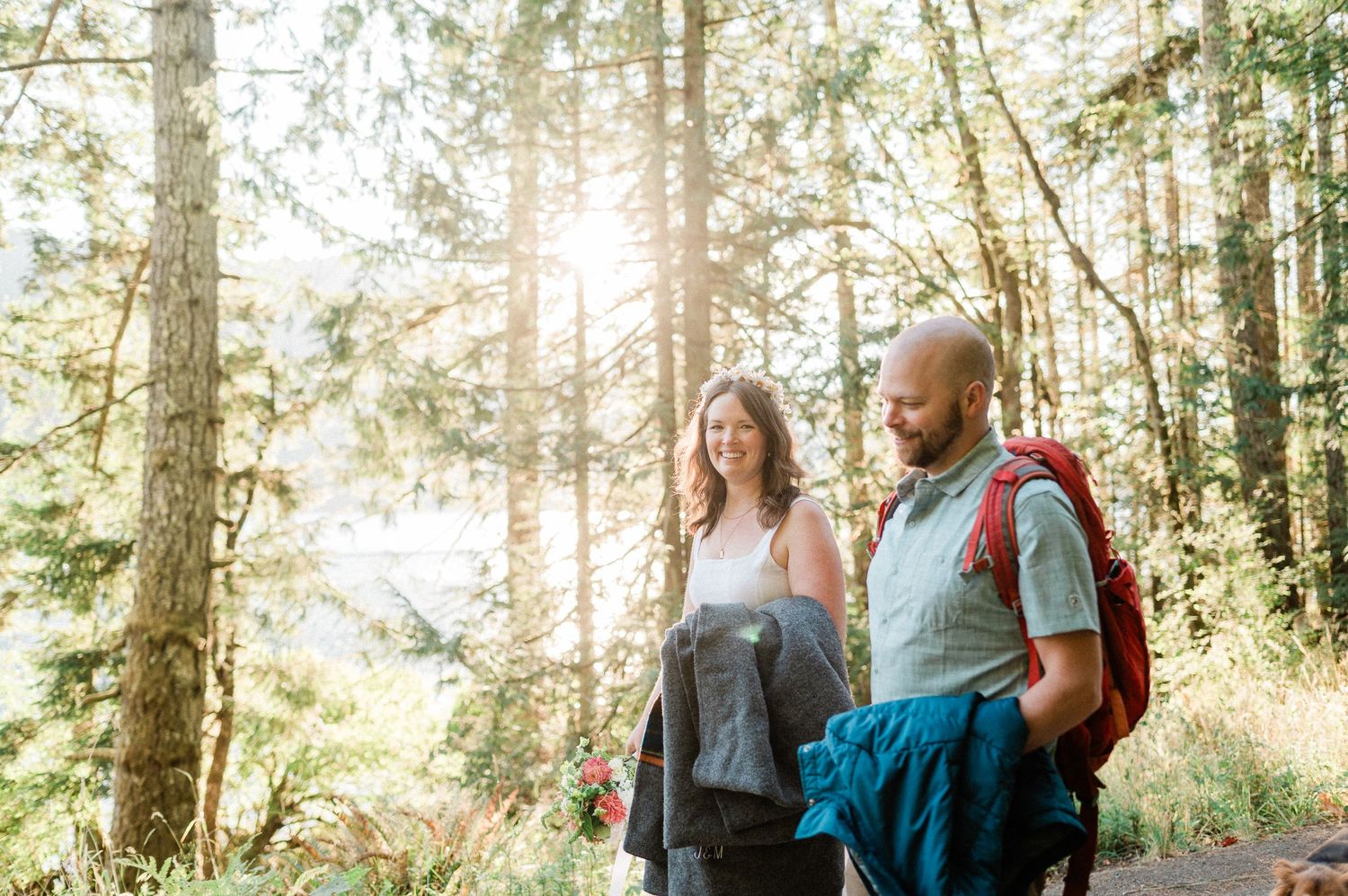 couple hiking together with sun shinning through trees behind them