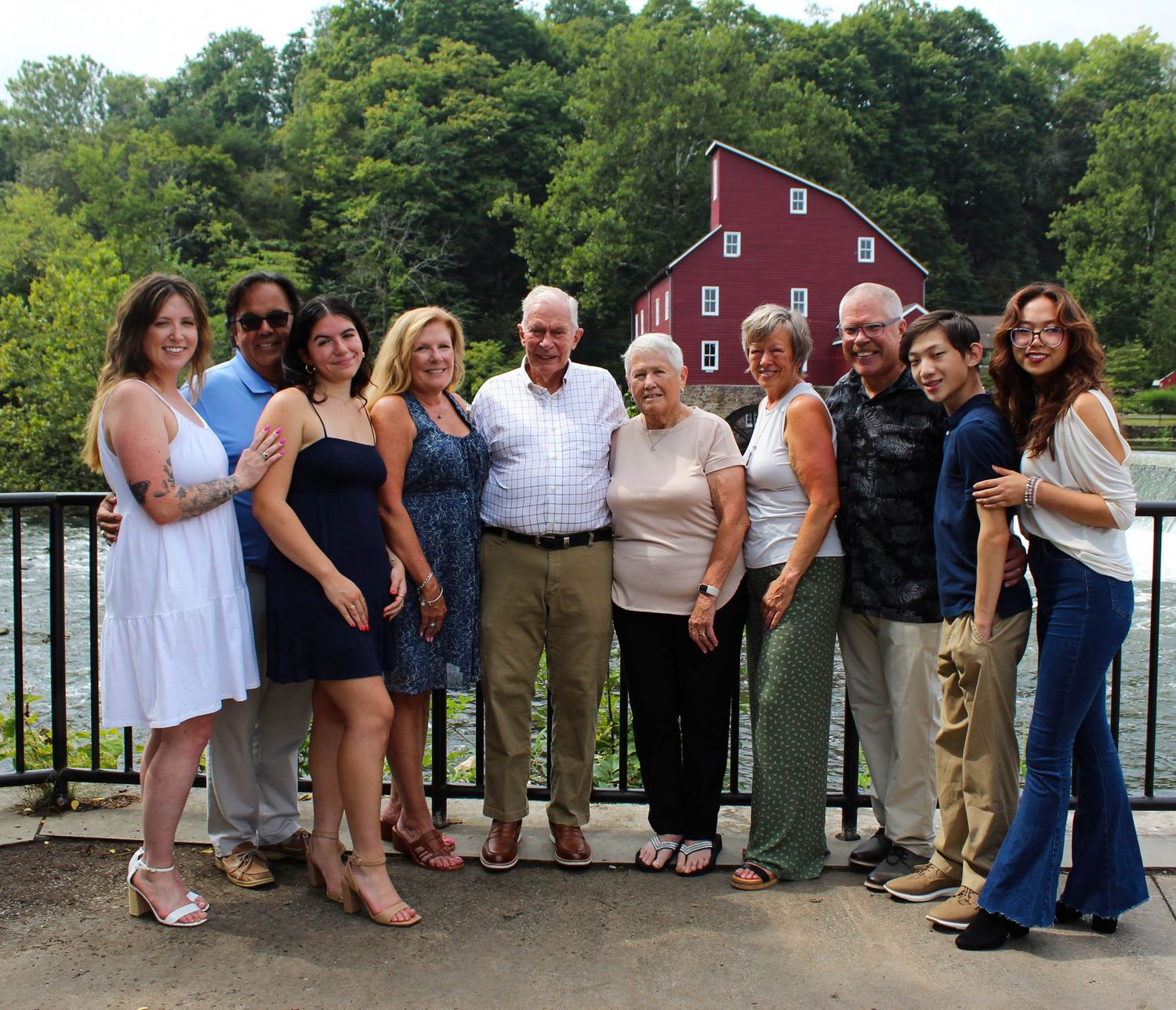 Family gathering on a deck overlooking a historic red mill building and waterway.