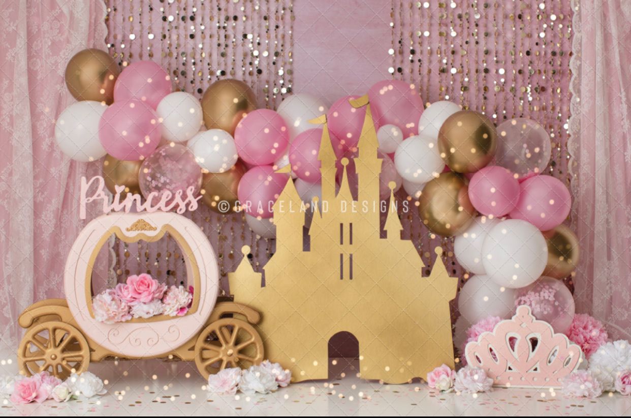 Pink and gold princess-themed party backdrop with balloon garland, castle cutout, carriage decor and sparkly curtain.