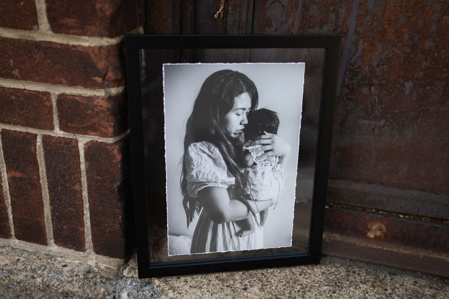Black and white portrait photo in a dark frame leaning against a brick wall.