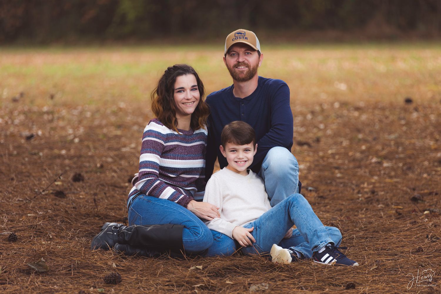 A relaxed family portrait taken outdoors on brown autumn ground.